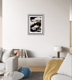 Ein modernes Wohnzimmer in neutralen Tönen mit einem weißen Sofa, einer kuscheligen gelben Strickdecke, einer weißen Lampe mit Holzfuß, Büchern auf einem niedrigen Schrank und "Zeichnungen & Reduktion II" der Künstlerin Conny Wachsmann als abstrakte Wandkunst.