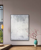 Ein modernes, minimalistisches Zimmer zeigt "Stiller Spaziergang" von Conny Wachsmann, Künstlerin, an einer hellen Wand - gepaart mit einer hängenden Laterne und einer türkisfarbenen Vase mit rosa Blüten auf dem Holzboden. Natürliches Licht bringt Ruhe und Entspannung in den Raum.