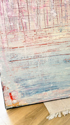 Vorschiedene Weiten" von Conny Wachsmann zeigt strukturierte rote, rosa und blaue Linien auf einem hellen Hintergrund in Kratztechnik. Das Kunstwerk lehnt an einer Wand über einem beigen Teppich auf einem Holzfußboden im Stil der artvergnuegen galerie.