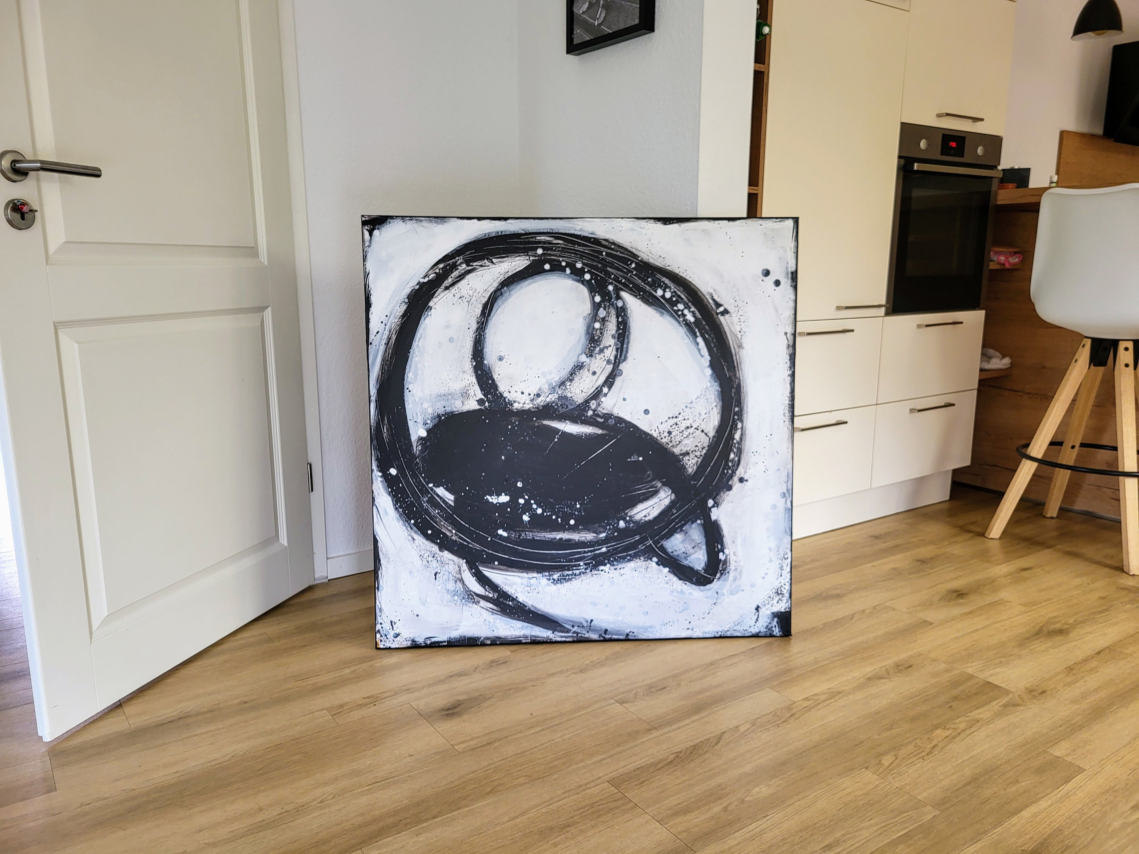 Das Kunstwerk "Nightswimming" von Conny Wachsmann mit schwarzen Kreisen und ovalen Pinselstrichen auf Weiß schmückt als individuelles Highlight eine moderne Küche mit Holzfußboden.