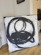 Nightswimming von Conny Wachsmann, Künstlerin, lehnt an einer Wand in einer modernen Küche. Kräftige, wirbelnde schwarze Pinselstriche, grobe Kreise und Farbspritzer heben sich von dem weißen Hintergrund ab.