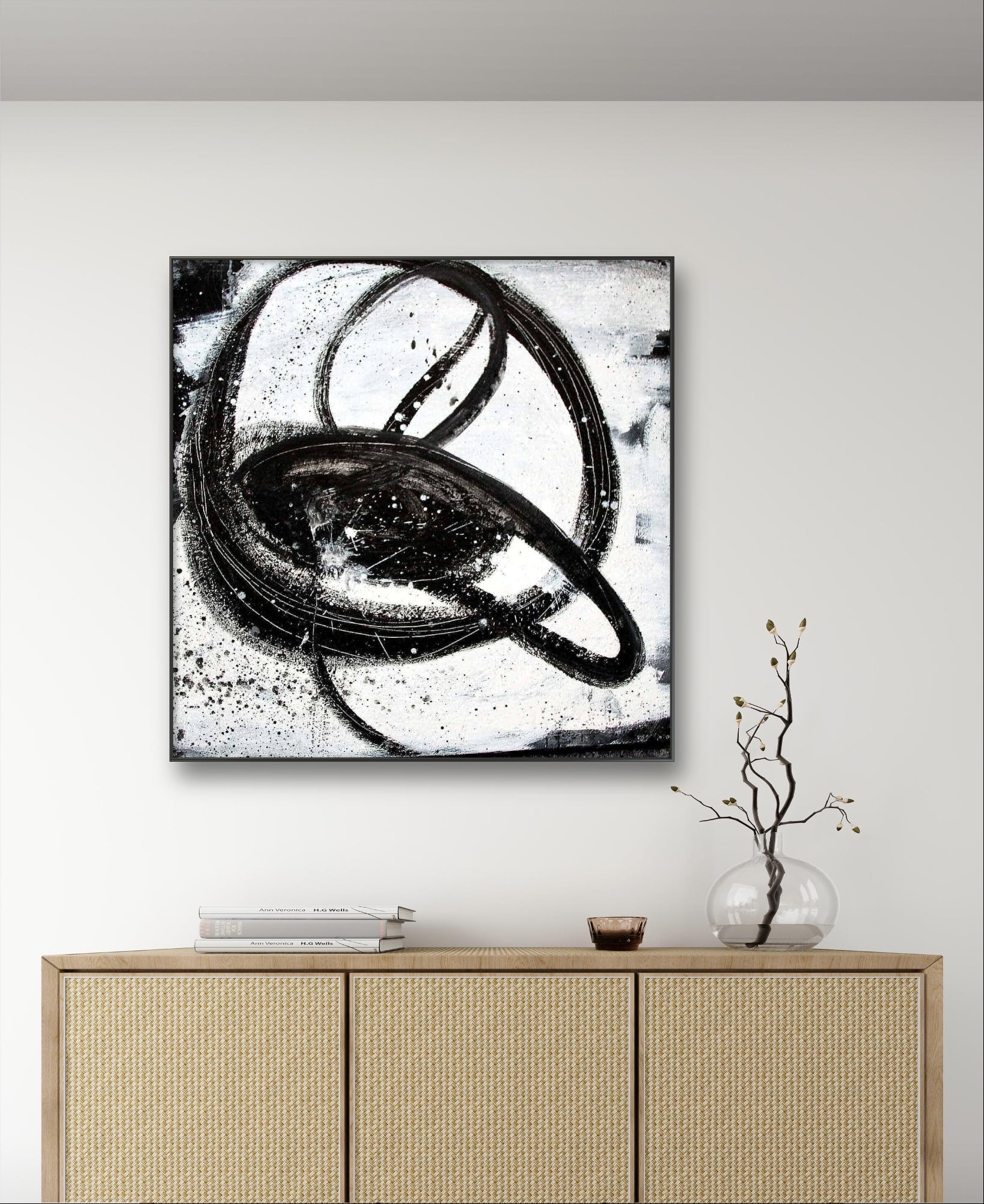 Ein minimalistisches Zimmer mit einem Sideboard aus hellem Holz, einer Glasvase mit kahlen Zweigen, einer kleinen Schale und "Nightswimming" von Conny Wachsmann, Künstlerin, einem großen abstrakten Gemälde mit kreisförmigen Formen, das an der weißen Wand darüber hängt.