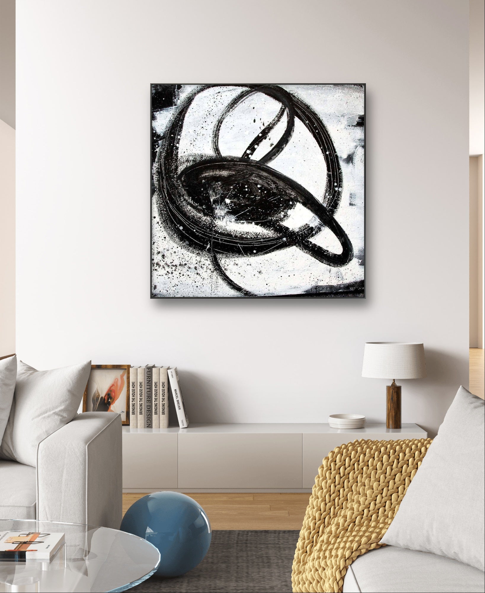 Ein modernes Wohnzimmer mit einem weißen Sofa, einer beigen Strickdecke, einem runden blauen Hocker und einem weißen Schrank. Über dem Schrank hängt "Nightswimming" von Conny Wachsmann, Künstlerin - ein markantes abstraktes Gemälde mit wirbelnden Pinselstrichen.