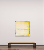 Eine minimalistische Galerie mit einer Holzbank steht „Küstenzauber II“ von Conny Wachsmann gegenüber, einer abstrakten Landschaft in sanftem Gelb, Weiß und Hellblau, die an einer weißen Wand über dem polierten Holzboden hängt.