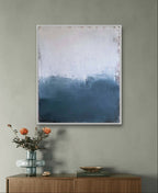 In einem minimalistischen Zimmer stehen ein hölzernes Sideboard, eine Glasvase mit orangefarbenen Blumen, Dekorationsgegenstände und "Ein Ausweg" von Conny Wachsmann, Künstlerin - ein abstraktes Kunstwerk in Paynesgrau und Blau - an der grauen Wand.