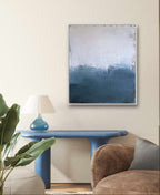 In einem minimalistischen Wohnzimmer stehen ein blauer Konsolentisch mit einer Glaslampe, eine Pflanze, ein brauner Sessel und "Ein Ausweg" von Conny Wachsmann - ein abstraktes Kunstwerk in Paynesgrau und Weiß - an einer hellen, strukturierten Wand.