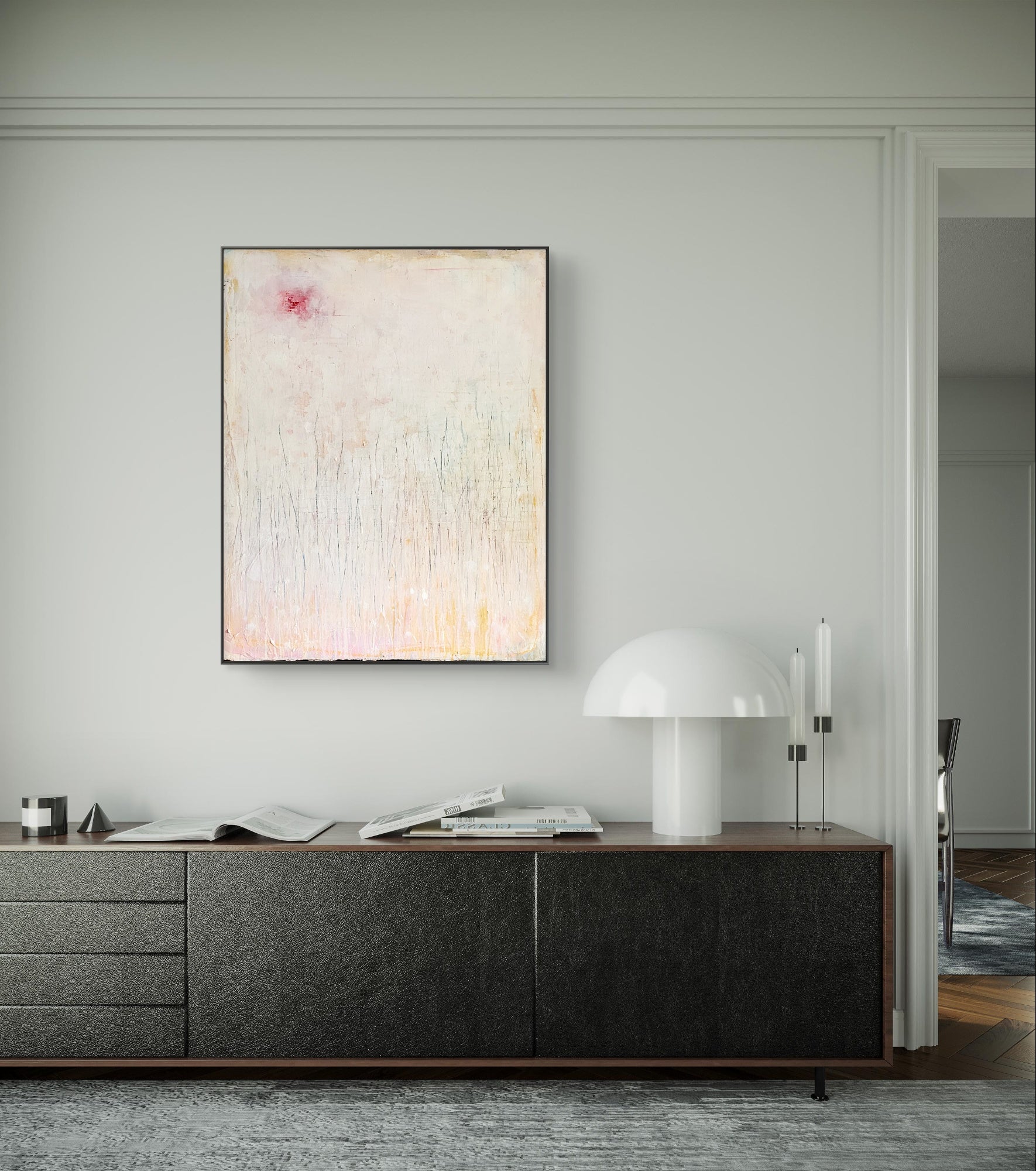 Minimalistisches Wohnzimmer mit niedrigem, dunklem Sideboard, „Gedankenregen“ von Conny Wachsmann, Künstlerin in sanften Pastelltönen an der Wand, dazu eine moderne weiße Tischleuchte, Kerzen, Bücher und Deko-Objekte übersichtlich arrangiert.