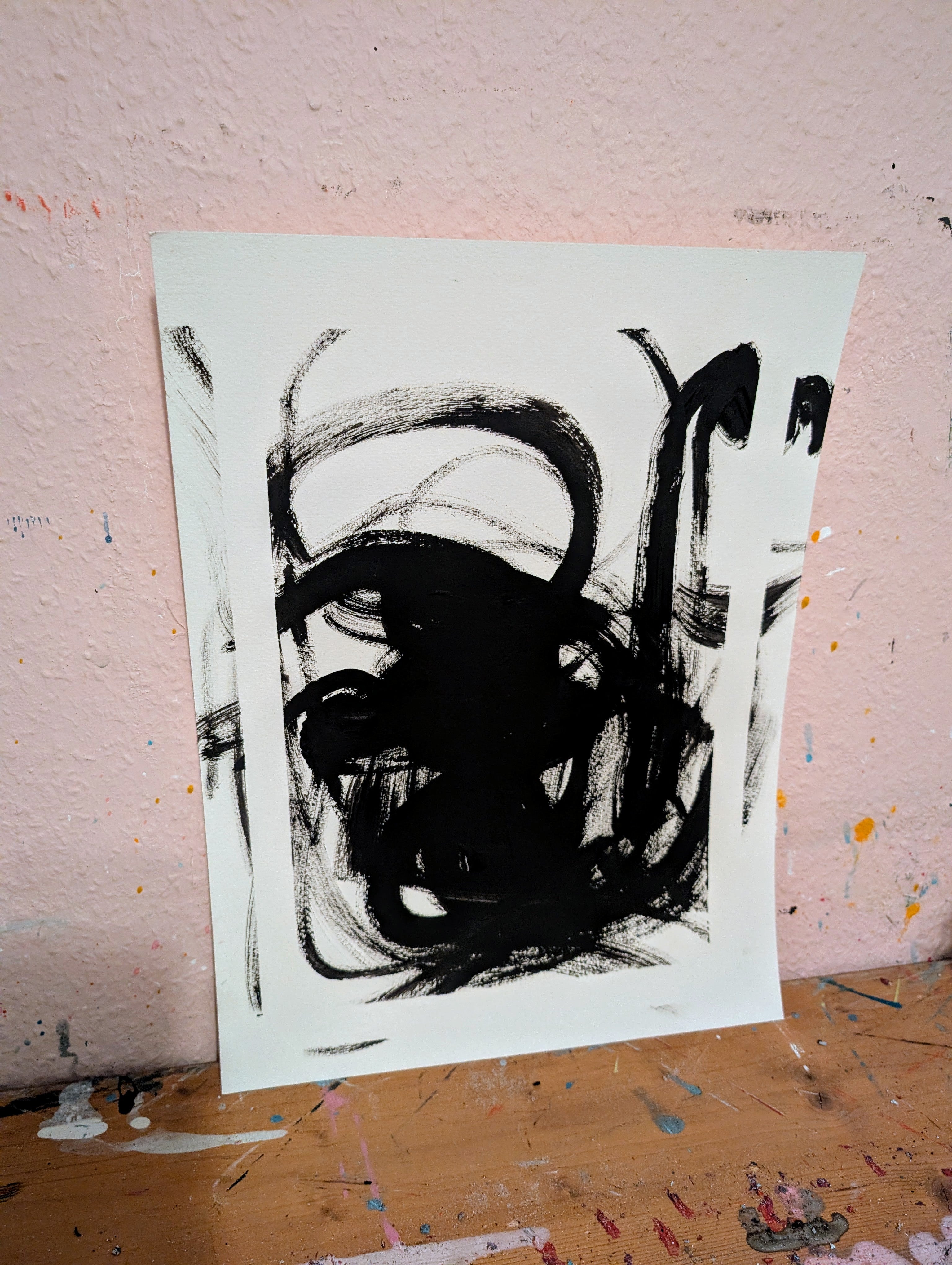 Zeichnungen & Reduktion IV" von Conny Wachsmann, Künstlerin: Eine minimalistische Originalzeichnung in Schwarz-Weiß mit abstrakten Pinselstrichen, angelehnt an eine strukturierte rosa Wand auf einem holzfarbenen Untergrund.