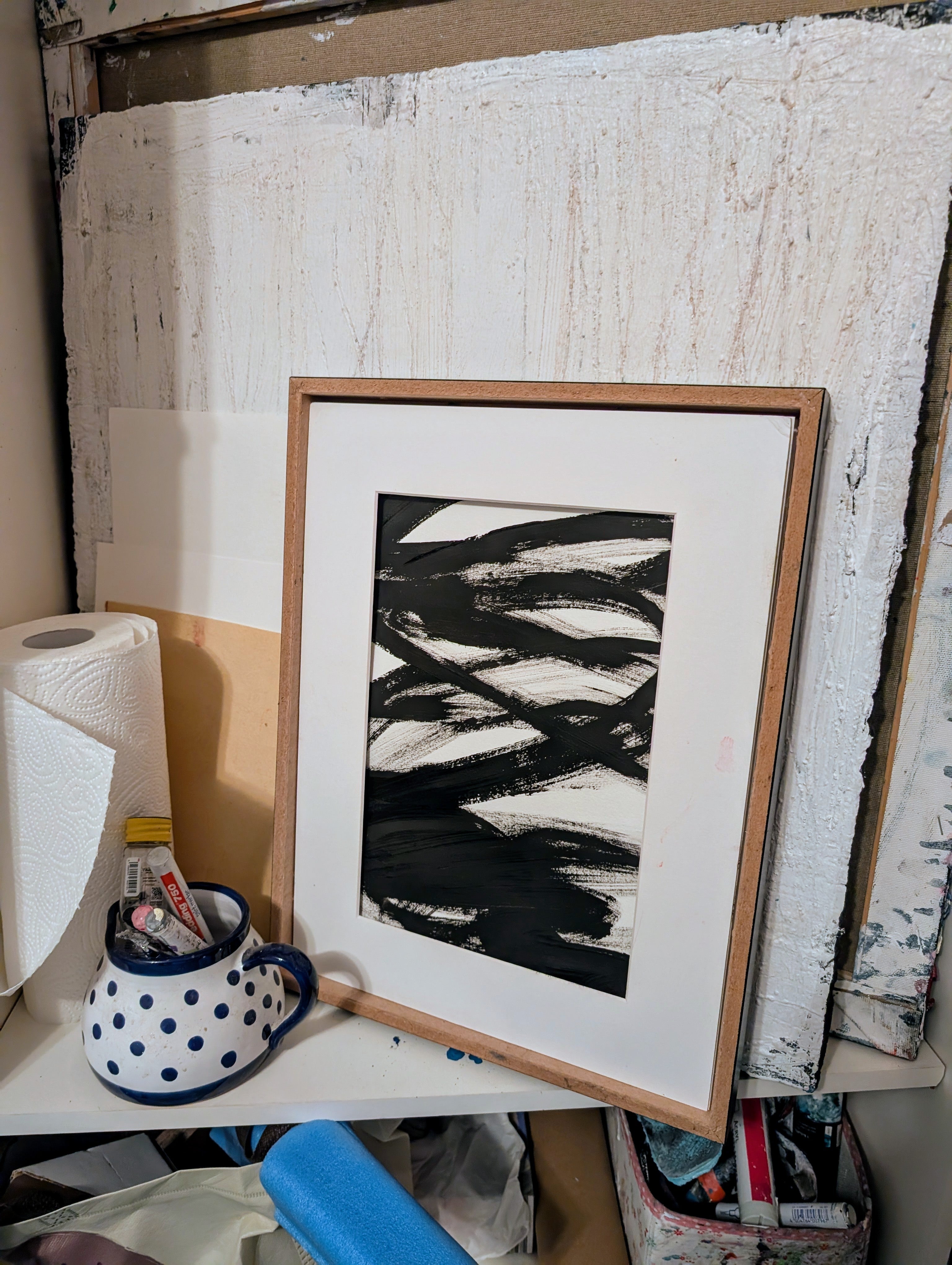 Zeichnungen & Reduktion III von Conny Wachsmann, Künstlerin, lehnt an einer strukturierten Leinwand inmitten einer Rolle Papierhandtücher, einem blau-weiß gepunkteten Becher, der mit Kunstzubehör gefüllt ist - eine ideale Szene für Fans minimalistischer Kunst.