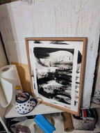 Das gerahmte Kunstwerk "Zeichnungen & Reduktion II" von Conny Wachsmann ruht auf einem Regal mit einer gepunkteten Teekanne, Papiertüchern und Kunstzubehör vor einer strukturierten Wand in einem Künstleratelier.