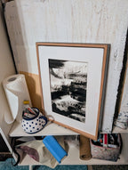 Das Kunstwerk "Zeichnungen & Reduktion II" von Conny Wachsmann, Künstlerin, ist gerahmt und lehnt an einer strukturierten Wand in einem Regal neben einer Rolle Papierhandtücher, einem blauen Tuch, einem gepunkteten Becher mit Pinseln und diversem Kunstzubehör.