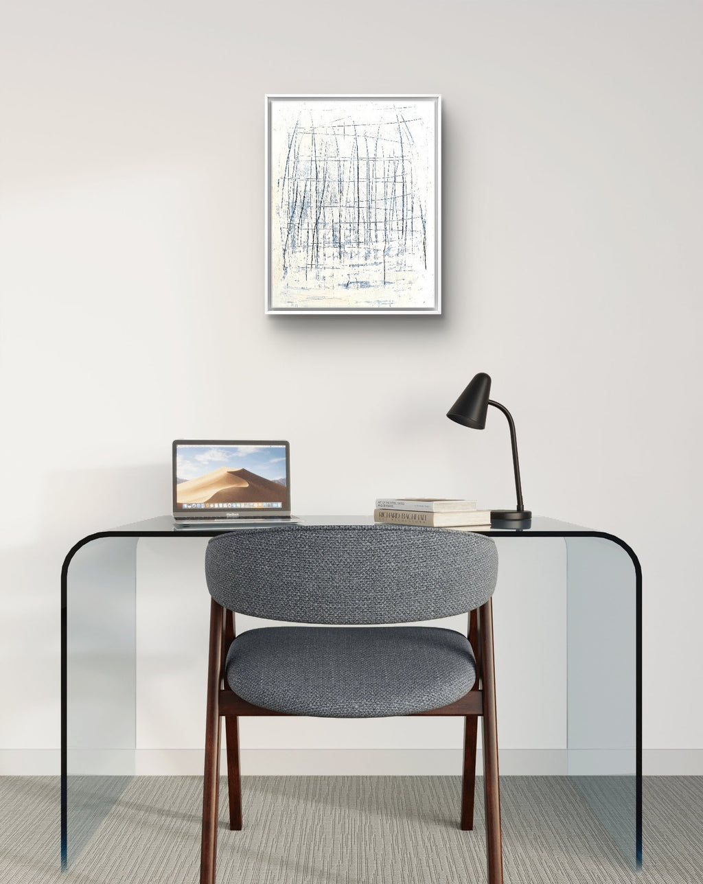 Ein minimalistischer Arbeitsplatz mit Glasschreibtisch, grauem Stuhl, Laptop, Schreibtischlampe und Büchern. An der hellen Wand darüber hängt „Feldlinien“ von Conny Wachsmann – ein abstraktes blau-weißes Acrylbild auf Leinwand mit feiner Linienstruktur.