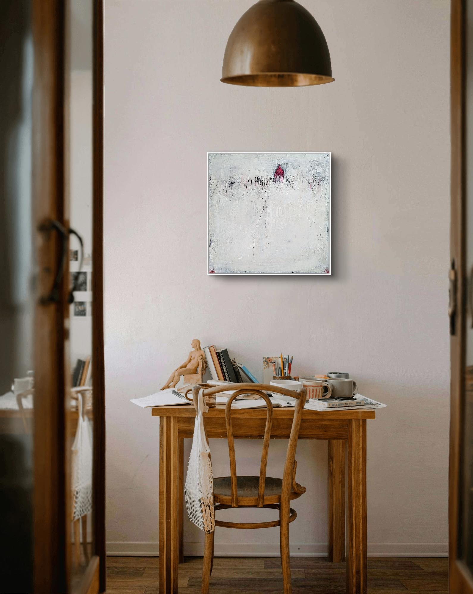 Ein Holzschreibtisch mit Künstlerutensilien und einer Tasse steht an einer hellen Wand, über der „Stille Spur“ von Conny Wachsmann hängt. Ein Holzstuhl und eine Kupferpendelleuchte runden diesen gemütlichen, künstlerischen Raum ab.