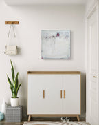 Ein moderner Eingangsbereich mit einem weißen Schrank aus Holz, einem karierten Pouf, einer großen grünen Pflanze, Wandhaken mit einer kleinen weißen Handtasche und „Stille Spur“ von Conny Wachsmann – einem strukturierten abstrakten Originalgemälde – an der Wand.