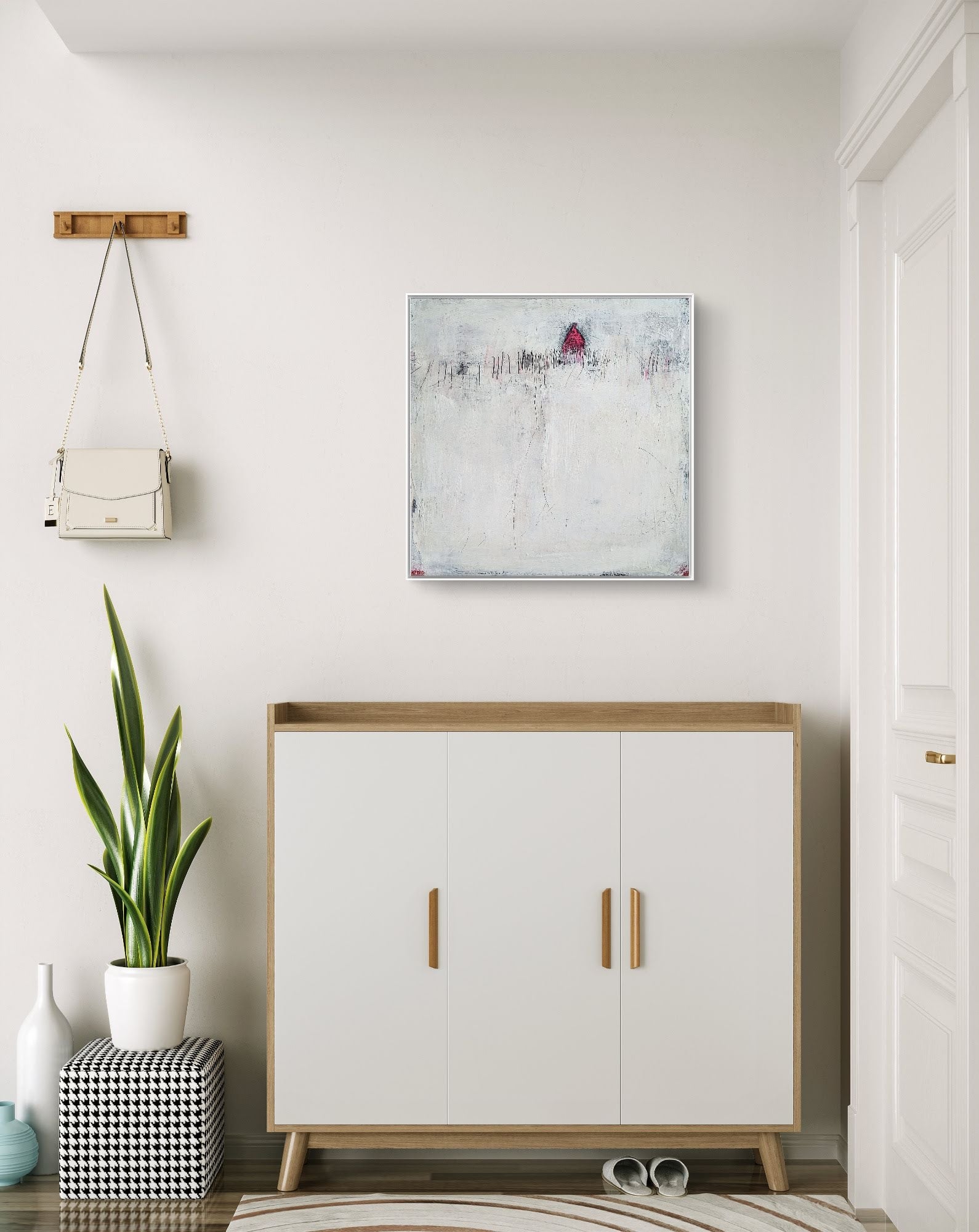 Ein moderner Eingangsbereich mit einem weißen Schrank aus Holz, einem karierten Pouf, einer großen grünen Pflanze, Wandhaken mit einer kleinen weißen Handtasche und „Stille Spur“ von Conny Wachsmann – einem strukturierten abstrakten Originalgemälde – an der Wand.