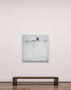 Eine minimalistische Galerie mit einer Holzbank steht gegenüber „Stille Spur“, einem abstrakten Originalgemälde von Conny Wachsmann in überwiegend weißen Tönen. Die strukturierte Oberfläche weist oben in der Mitte einen kleinen rot-schwarzen Akzent auf.