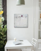 Ein kleiner weißer Tisch mit Stuhl, Kaffeetasse und zugeklapptem Laptop steht an einem hellen Fenster mit Pflanzen. Darüber hängt „Stille Spur“, ein abstraktes Originalgemälde mit strukturierter Oberfläche von Conny Wachsmann an der weißen Wand.