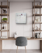 Ein modernes Homeoffice mit Holzregalen und einem grauen Stuhl an einem Holzschreibtisch. An der weißen Wand über dem Schreibtisch hängt „Stille Spur“ von Conny Wachsmann, Künstlerin – ein strukturiertes abstraktes Gemälde in hellen Farben.