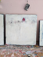 „Stille Spur“ von Conny Wachsmann ist ein minimalistisches abstraktes Originalgemälde mit überwiegend weißem Hintergrund, dezenten grauen Flecken und einem kleinen roten Dreieck oben in der Mitte. Darüber hängt eine alte Kamera an einer rosa Wand; Farbspritzer zieren den Boden.