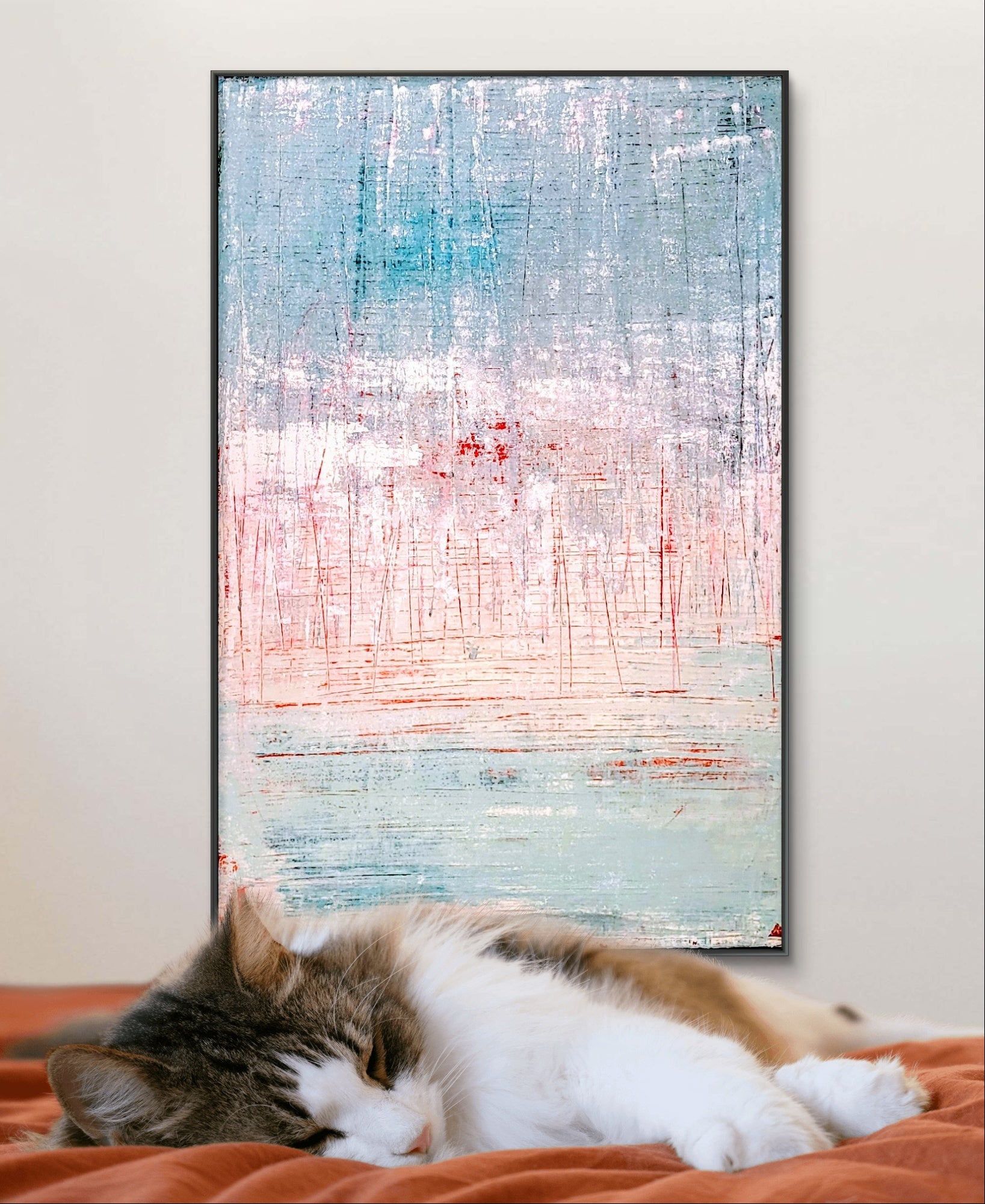 Eine gestromte, weiße Katze schläft auf einer orangefarbenen Decke vor einer Wand, die mit "Vorschiedene Weiten" der Künstlerin Conny Wachsmann mit blauen, rosa und weißen Pinselstrichen geschmückt ist.