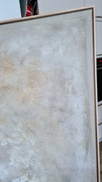 Das große gerahmte abstrakte Kunstwerk „Spurensuche“ von Conny Wachsmann in strukturierten Beige-, Grau- und Weißtönen lehnt an einer Küchentheke mit einem Backofen und roten Kanistern im Hintergrund.