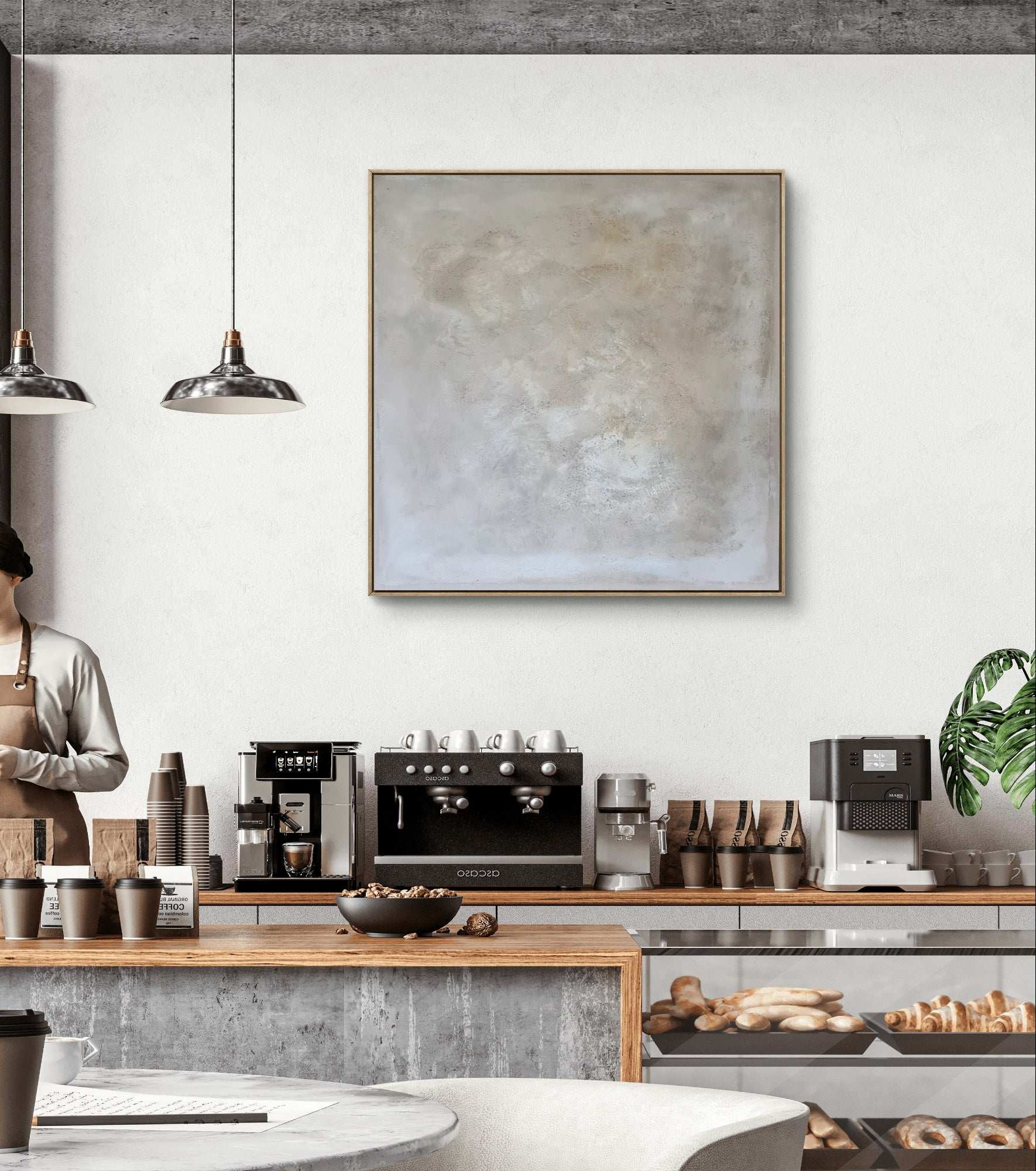 Modernes Café-Interieur mit neutralem Dekor, Kaffeemaschinen und Gebäck. An der weißen Wand hängt „Spurensuche“ von Conny Wachsmann, Künstlerin, in einem Schattenfugenrahmen.