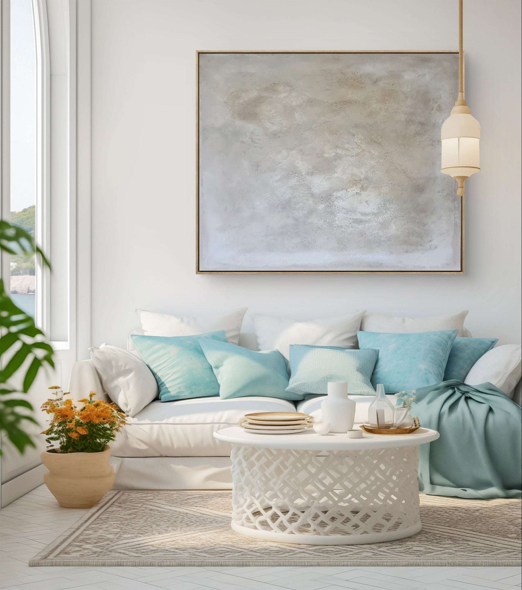 Ein helles Wohnzimmer mit einem weißen Sofa, blau-weißen Kissen, einer weichen Decke, einem runden weißen Couchtisch, Topfblumen, einer modernen Pendelleuchte und „Spurensuche“ von Künstlerin Conny Wachsmann in einem Schattenfugenrahmen an der Wand.