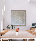 Heller, moderner Essbereich mit hellen Holztischen und Stühlen, roten Blumentöpfen, hohen grünen Pflanzen an der Wand und „Spurensuche“ von Conny Wachsmann in einem Schattenfugenrahmen an der weißen Wand.