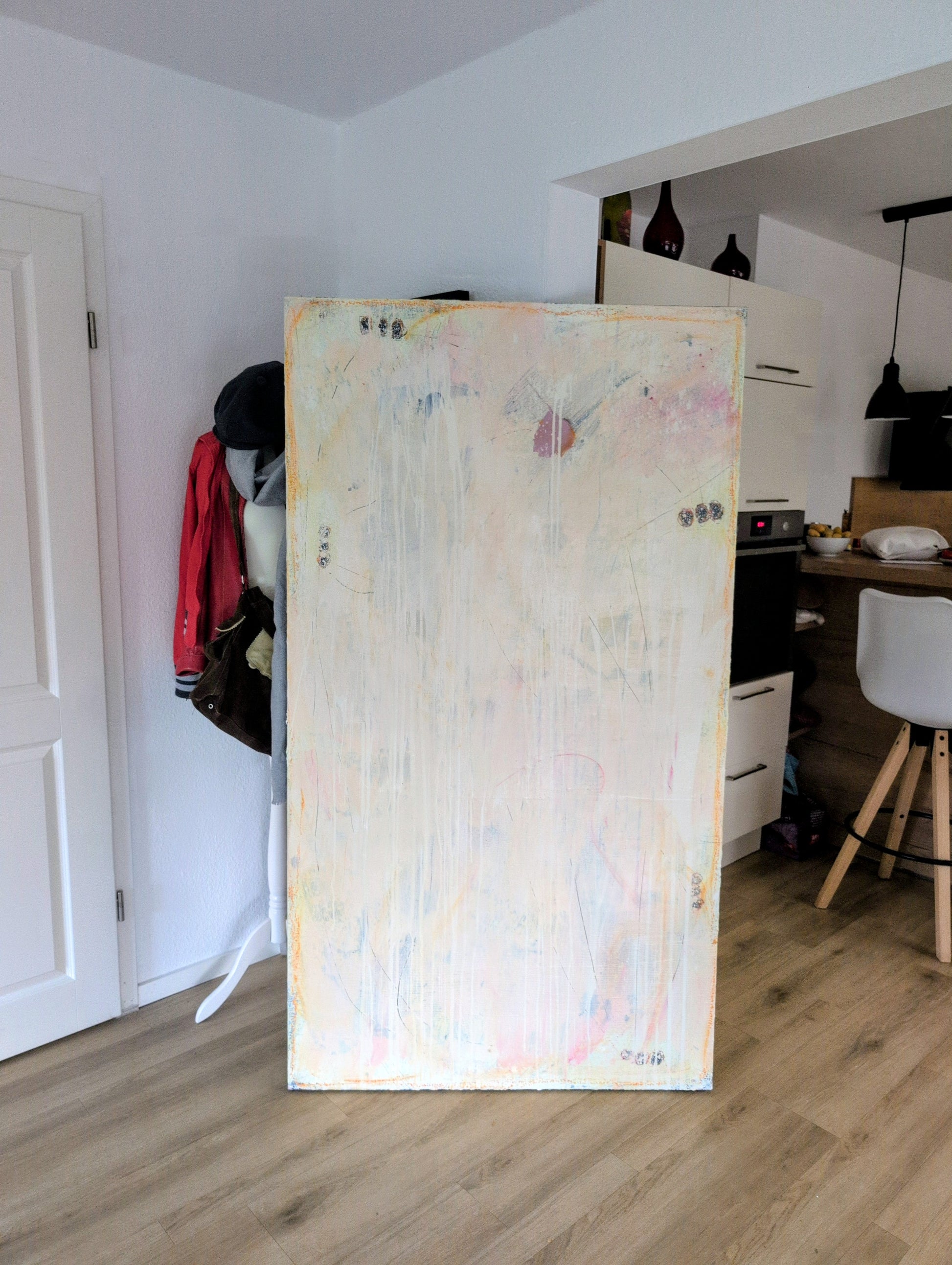 Das Bild "Eichhörnchentanz" von Conny Wachsmann lehnt zart getönt an der Wand eines modernen Raums. Dahinter ein Mannequin mit roter Jacke und Tasche nahe einer weißen Tür, im Hintergrund ist die Küche sichtbar.