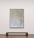 Minimalistische Kunstgalerie mit „Spurensuche“ von Conny Wachsmann, einem abstrakten Kunstwerk in neutralen Tönen, elegant gerahmt in einem Schattenfugenrahmen über einer einfachen Holzbank auf einem polierten Boden.