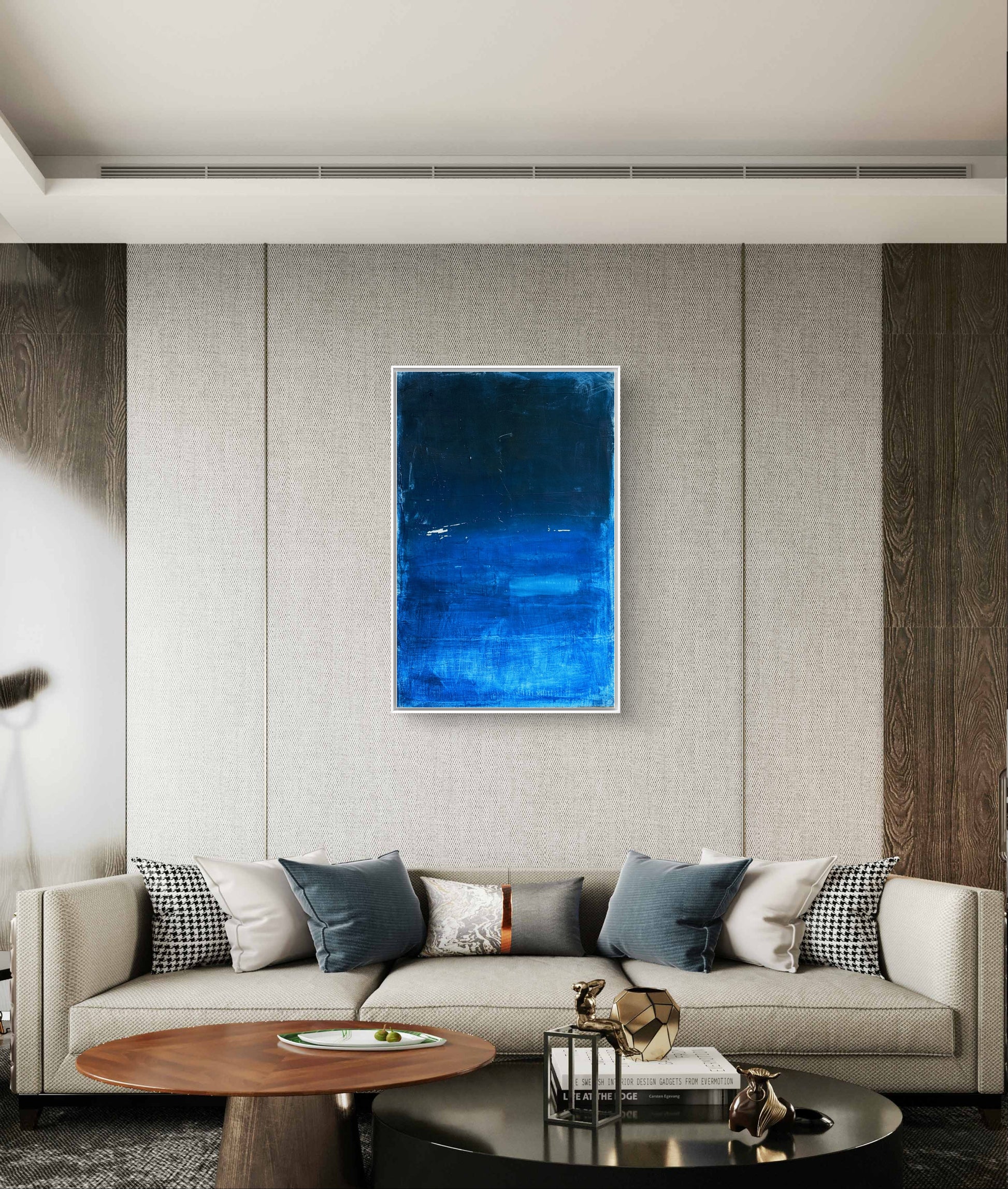 Ein modernes Wohnzimmer mit einem hellgrauen Sofa, blauen und neutralen Kissen, einem runden Couchtisch aus Holz und "Fjord", einem großen blauen abstrakten Gemälde der Künstlerin Conny Wachsmann, das an der strukturierten Wand über dem Sofa hängt.