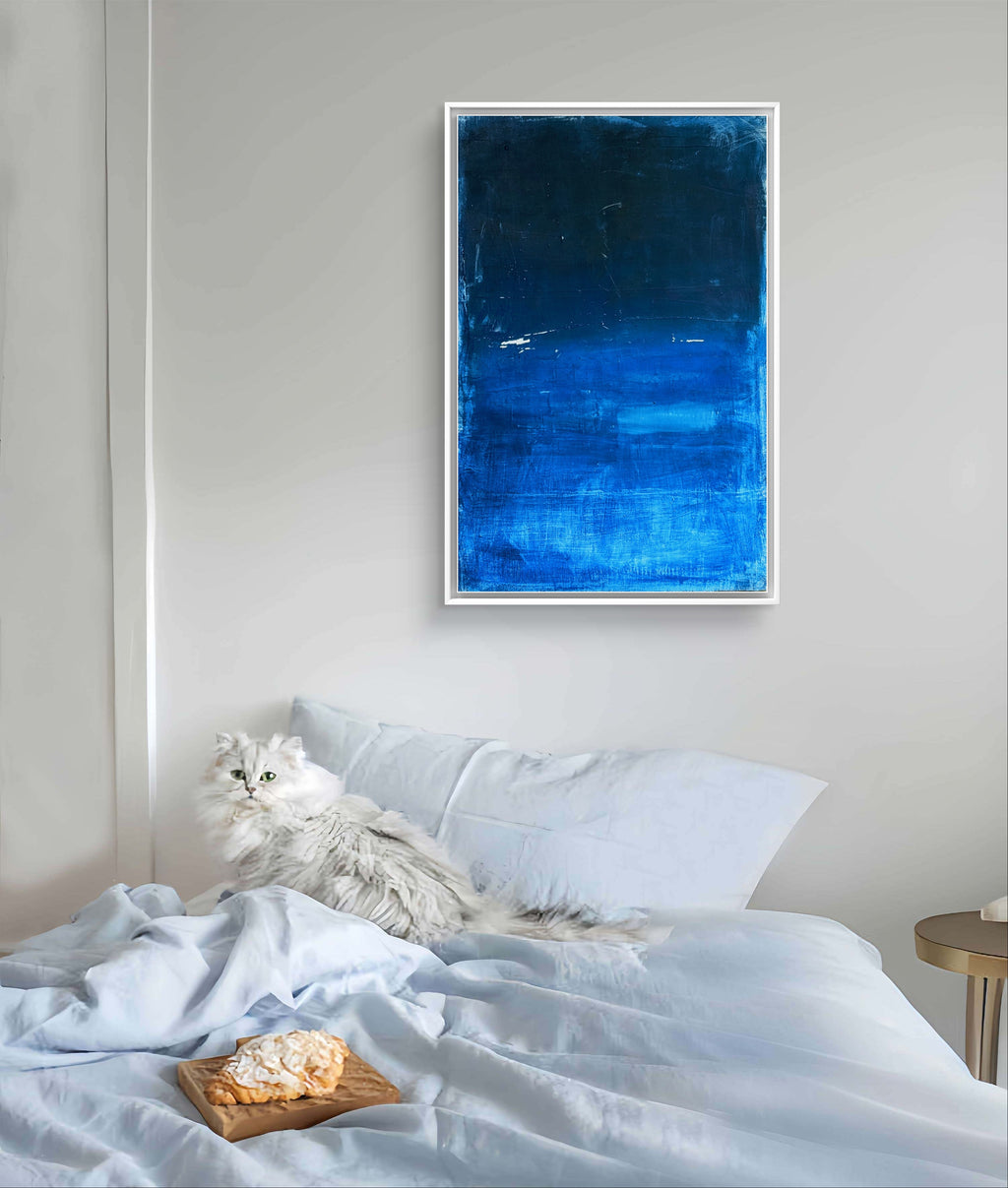Eine flauschige weiße Katze faulenzt auf einem ordentlich gemachten Bett mit hellblauer Bettwäsche. Darüber hängt "Fjord", ein signiertes Einzelstück Acryl auf Leinwand einer nordischen Landschaft der Künstlerin Conny Wachsmann. Ein Dessertteller steht daneben und vervollständigt die Szene.