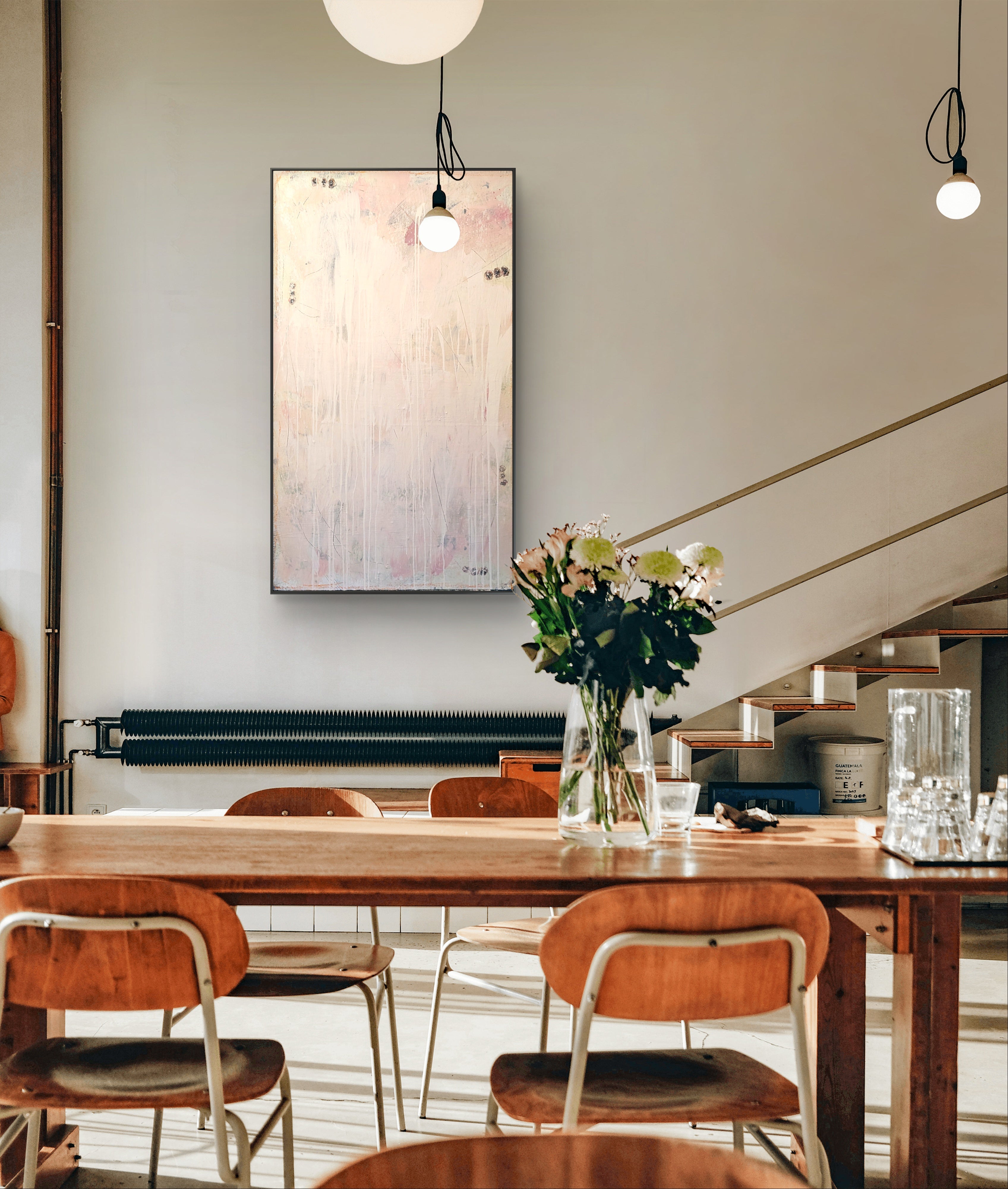 Ein moderner Essbereich mit Holzstühlen und -tisch, frischen Blumen, Gläsern, einer Treppe mit Goldgeländer und "Eichhörnchentanz" von Conny Wachsmann als Wanddekoration unter hängenden Pendelleuchten.