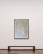 Eine minimalistische Galerie mit einer einfachen Holzbank steht gegenüber „Spurensuche“ von Conny Wachsmann, Künstlerin – ein großes Kunstwerk in sanften, gedämpften Tönen, elegant gerahmt in einem Schattenfugenrahmen an einer schlichten weißen Wand über einem Holzboden.