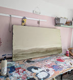 Zwischen Sommer und Herbst II", eine große Unikat-Leinwand der Künstlerin Conny Wachsmann mit abstrakter Spachtelarbeit in neutralen Tönen, liegt auf einem unordentlichen, mit Farbspritzern übersäten Arbeitstisch; Regale und Kunstzubehör säumen die weiß-rosa Wand dahinter.