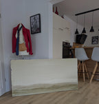 Zwischen Sommer und Herbst II", ein großes abstraktes Gemälde von Conny Wachsmann, lehnt an der Wand in einer modernen Küche. Daneben steht eine Schaufensterpuppe mit roter Jacke, blauer Krawatte und hellbrauner Tasche neben weißen Schränken und Barhockern.