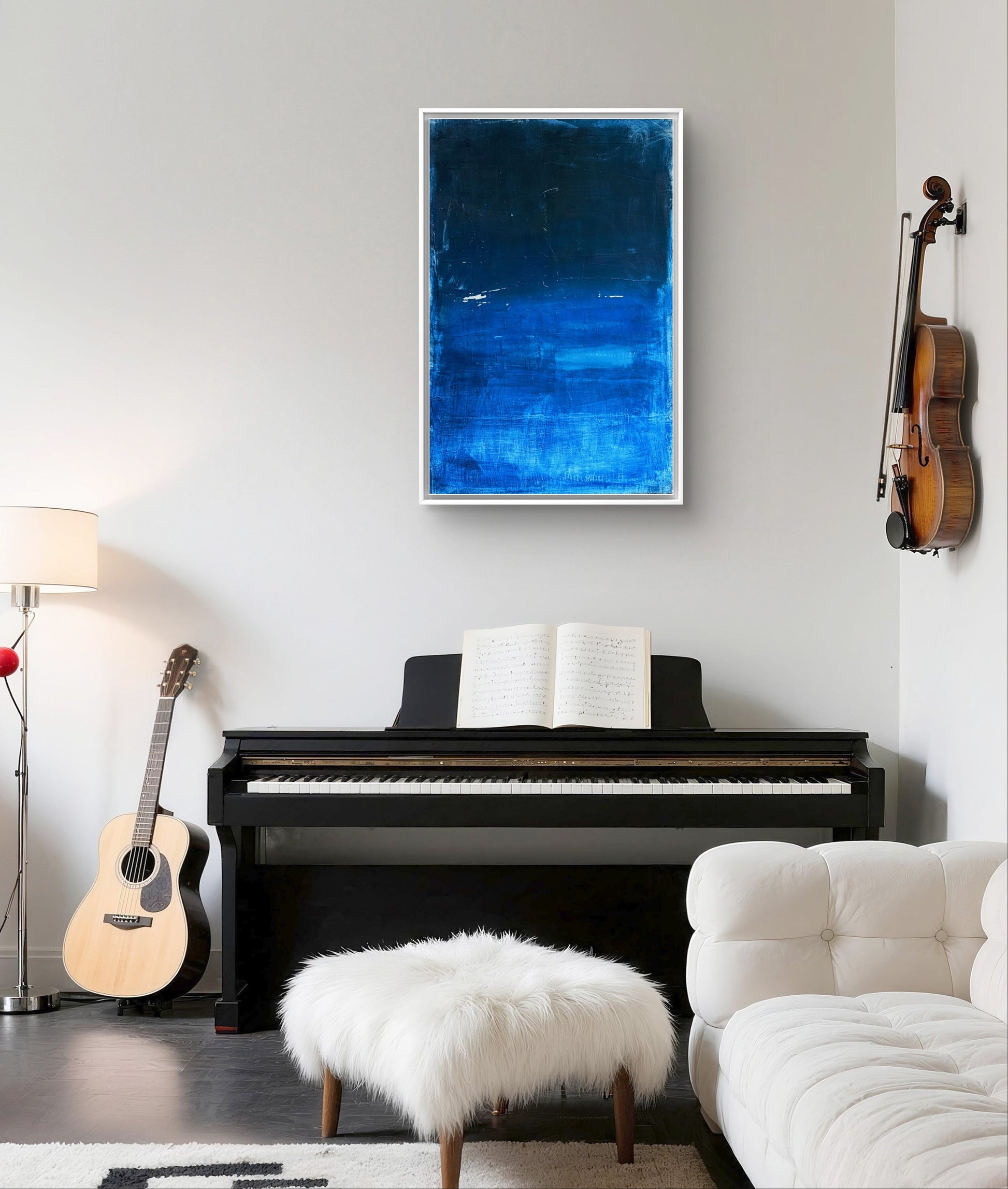 In einem modernen Wohnzimmer steht ein schwarzes Klavier mit geöffneten Notenblättern und einer Gitarre daneben. Darüber hängt "Fjord" von Conny Wachsmann, ein abstraktes Kunstwerk in Blau, das von nordischen Landschaften inspiriert ist. Eine Geige und ein weißer, pelziger Ottoman vervollständigen die Szene.