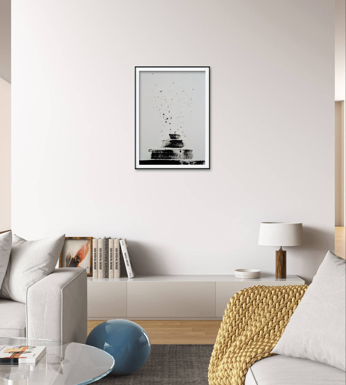 Ein modernes Wohnzimmer mit einem niedrigen weißen Schrank, Büchern, einem runden blauen Hocker, einer beigen Strickdecke und einer Tischlampe. Über dem Schrank hängt die Arbeit "Zeichnungen & Reduktion V" von Conny Wachsmann, die einen auffälligen Akzent im Raum setzt.